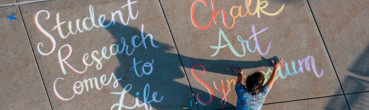 Someone writing the words Chalk Art Symposium.